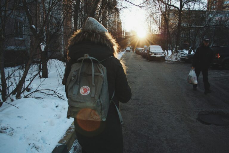 Woman in black jacket and brown backpack standing on road during daytime