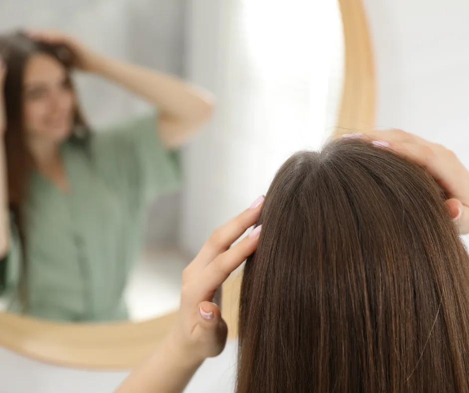 Femme qui vérifie ses racines grasses devant un miroir en passant la main dans ses cheveux bruns